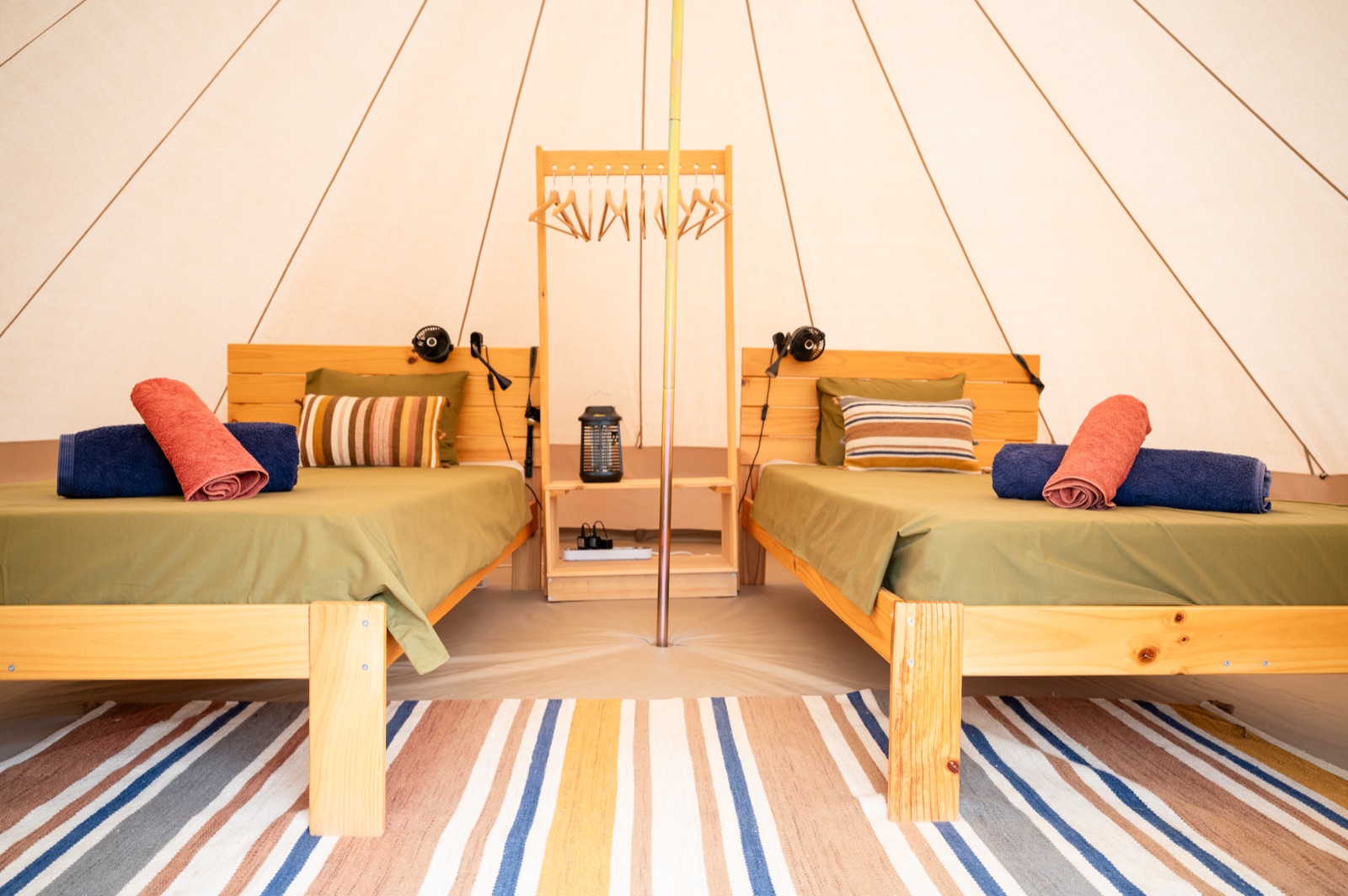 Inside a twin bell tent with two cosy beds, rugs and warm tones