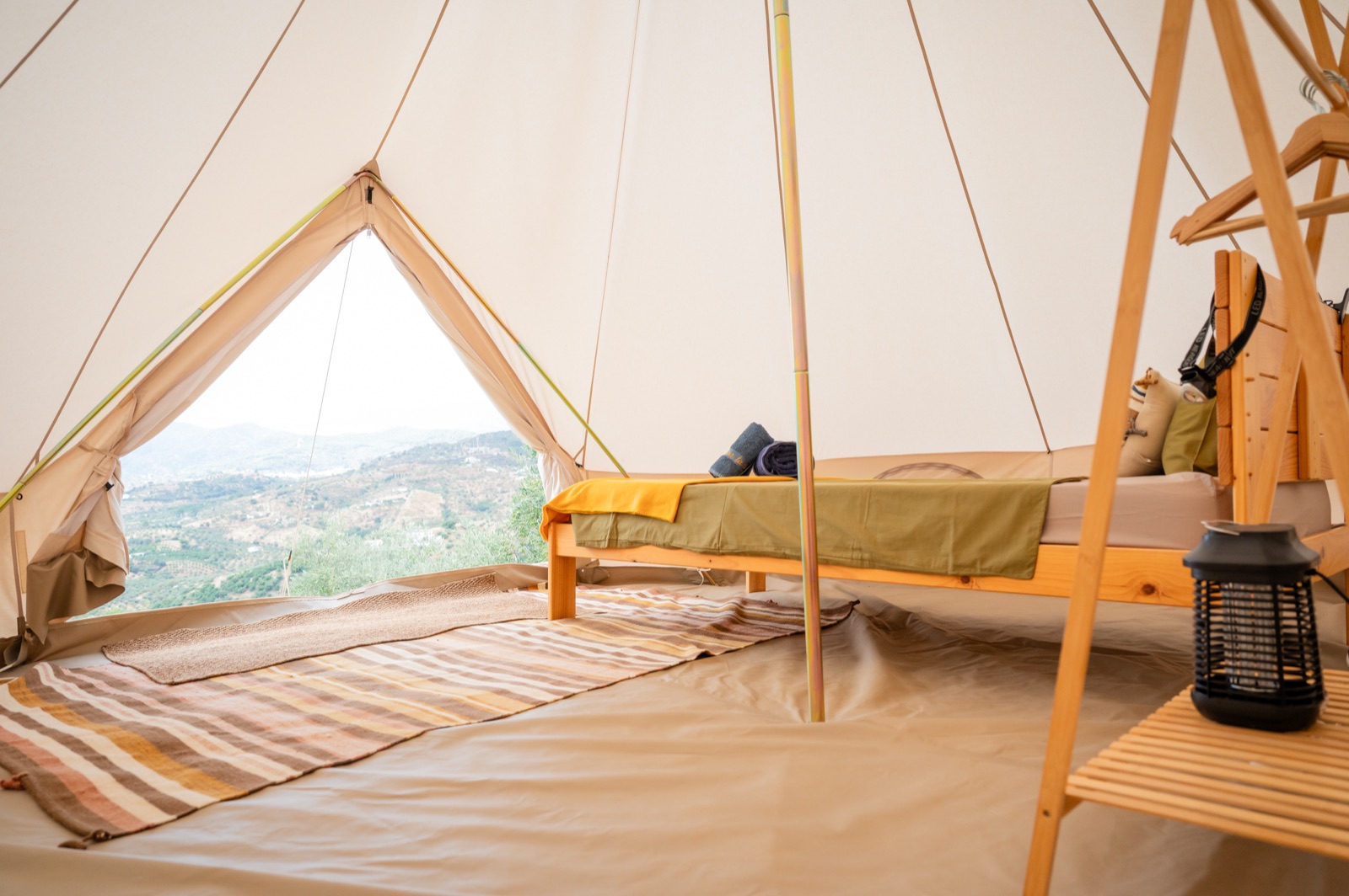 Inside a single bell tent with a bed and a view across the olive valley